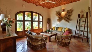 A cozy living room with a curved window, wooden furniture, and a decorative wall piece.