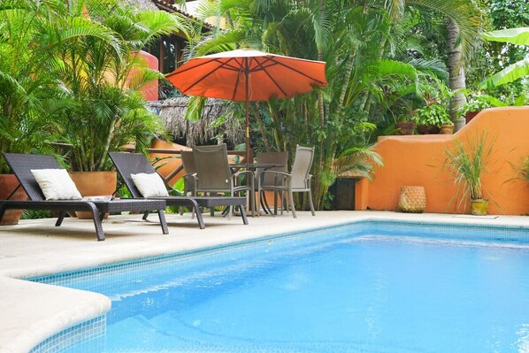 Un espace aménagé au bord de la piscine, avec des chaises longues, une table et un parasol.