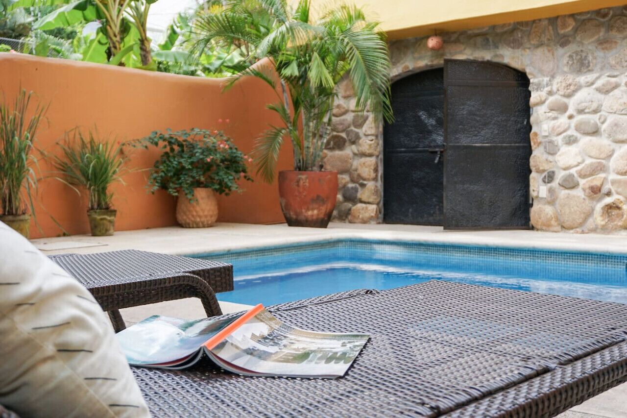 A pool area with lounge chairs, potted plants, and a stone wall.