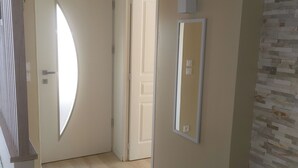 Een gang met een houten vloer, beige wanden en een deur met een ronde spiegel.