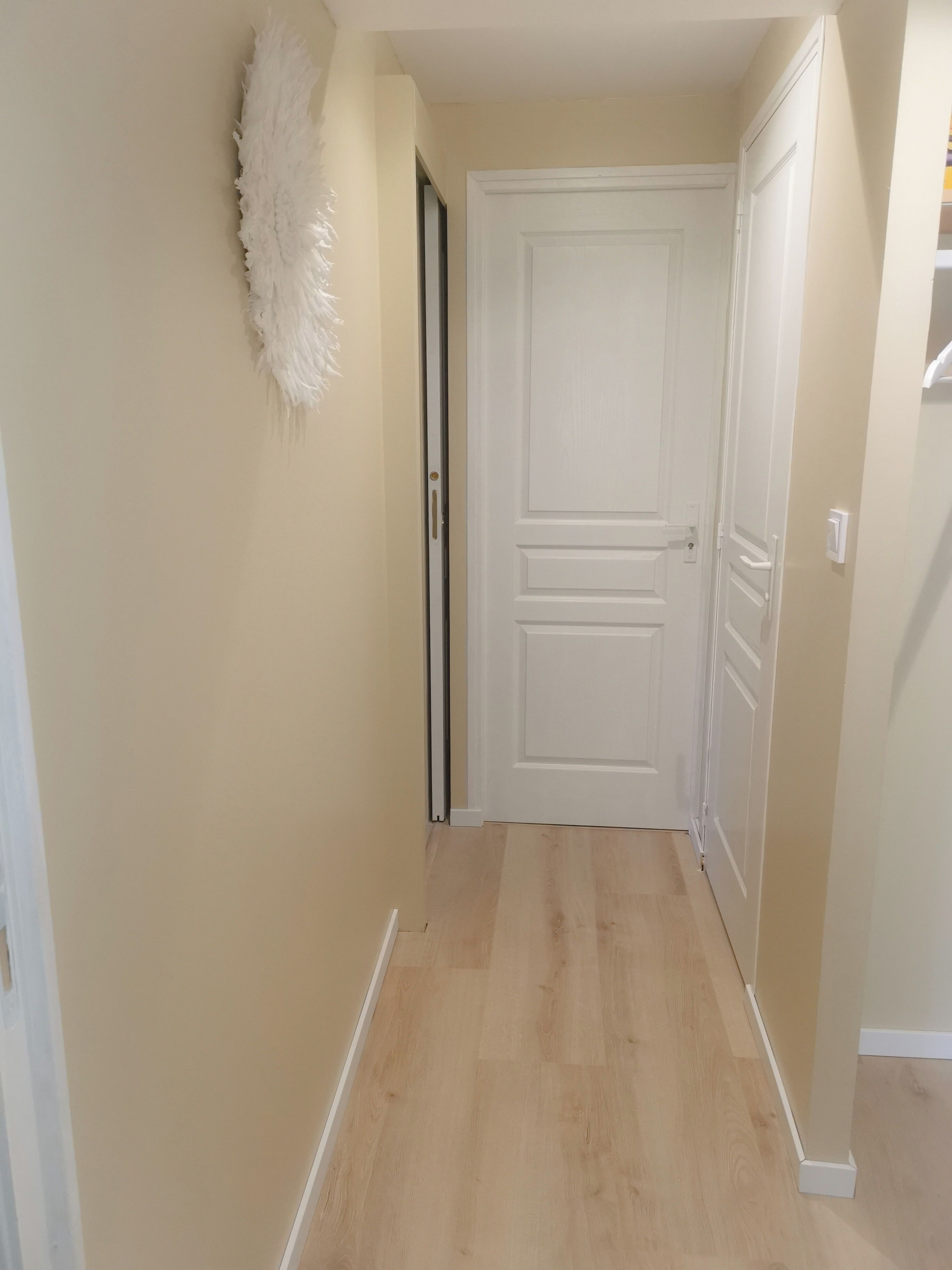 A hallway with a white door, beige walls, and wooden flooring.