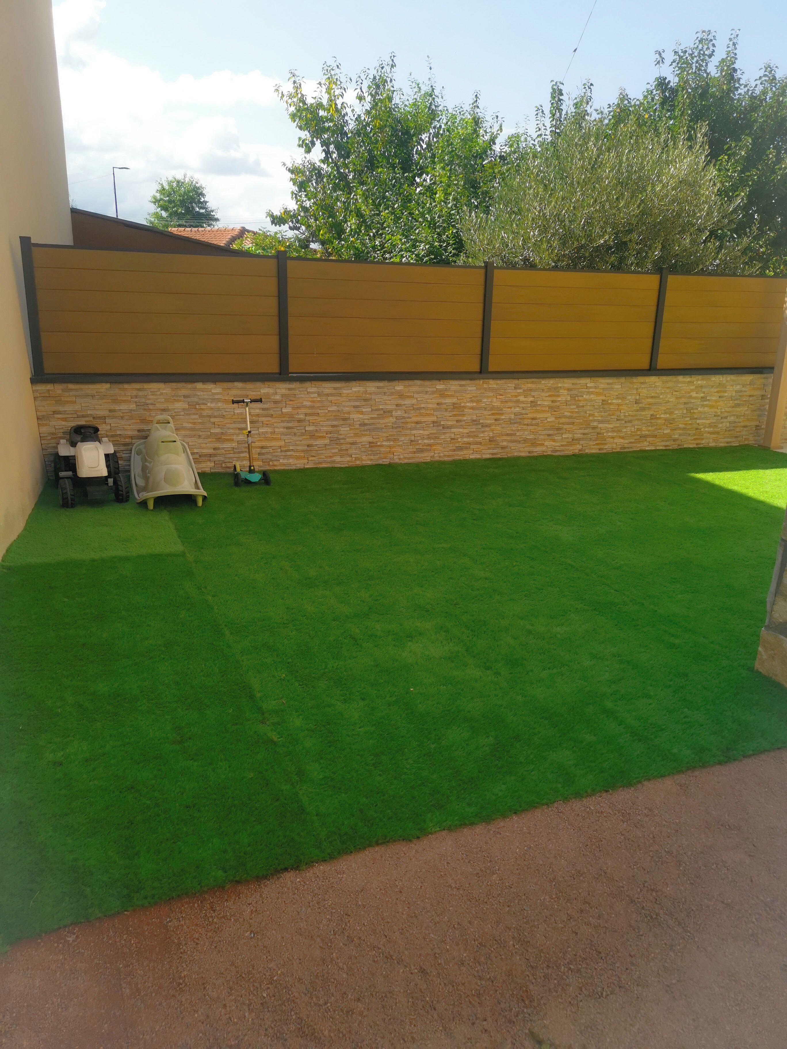A backyard with artificial grass, a wooden fence, and a scooter.