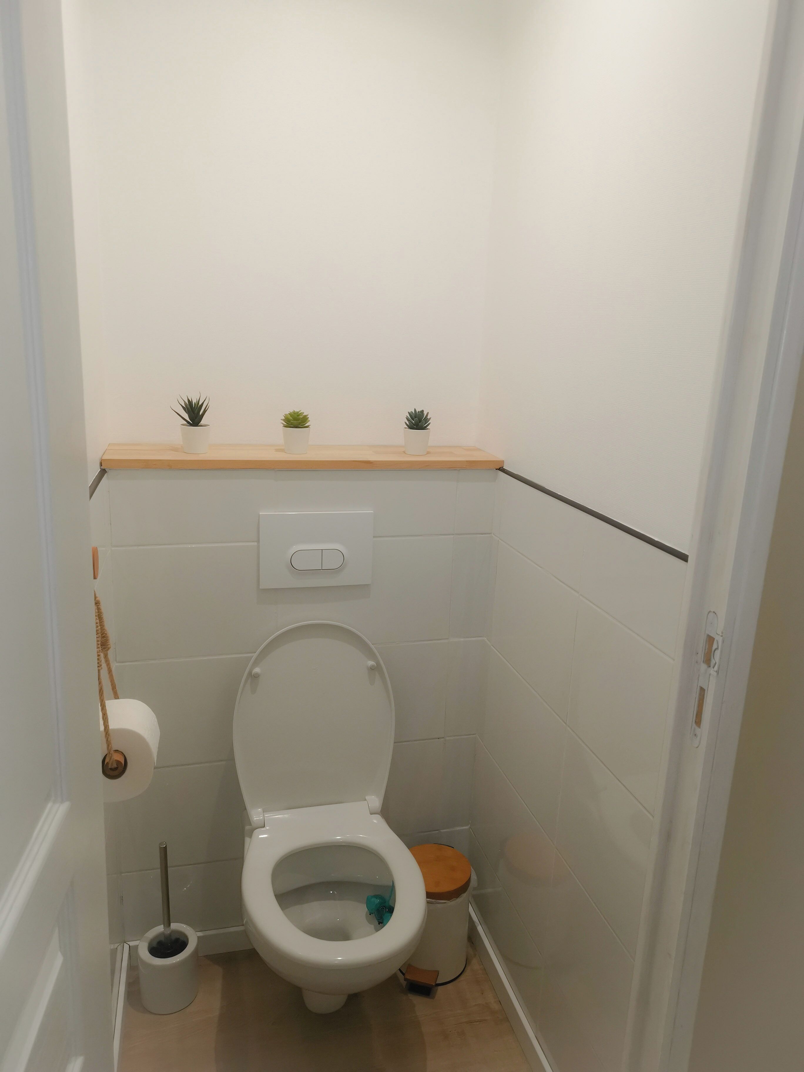 A small, clean bathroom with a toilet, bidet, and two small potted plants on a shelf above the toilet.