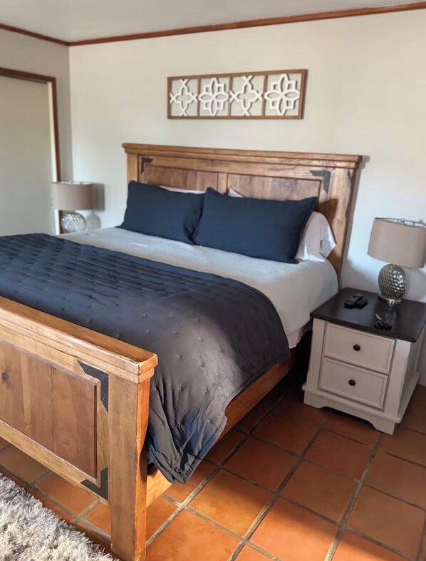 A bedroom with a wooden bed, a nightstand, a lamp, and a decorative wall piece.