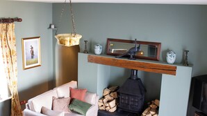 A living room with a sofa, a fireplace with logs, a television, and a hanging light fixture. - Hill House Lodge, overlooking the Rock of Cashel (Cashel)