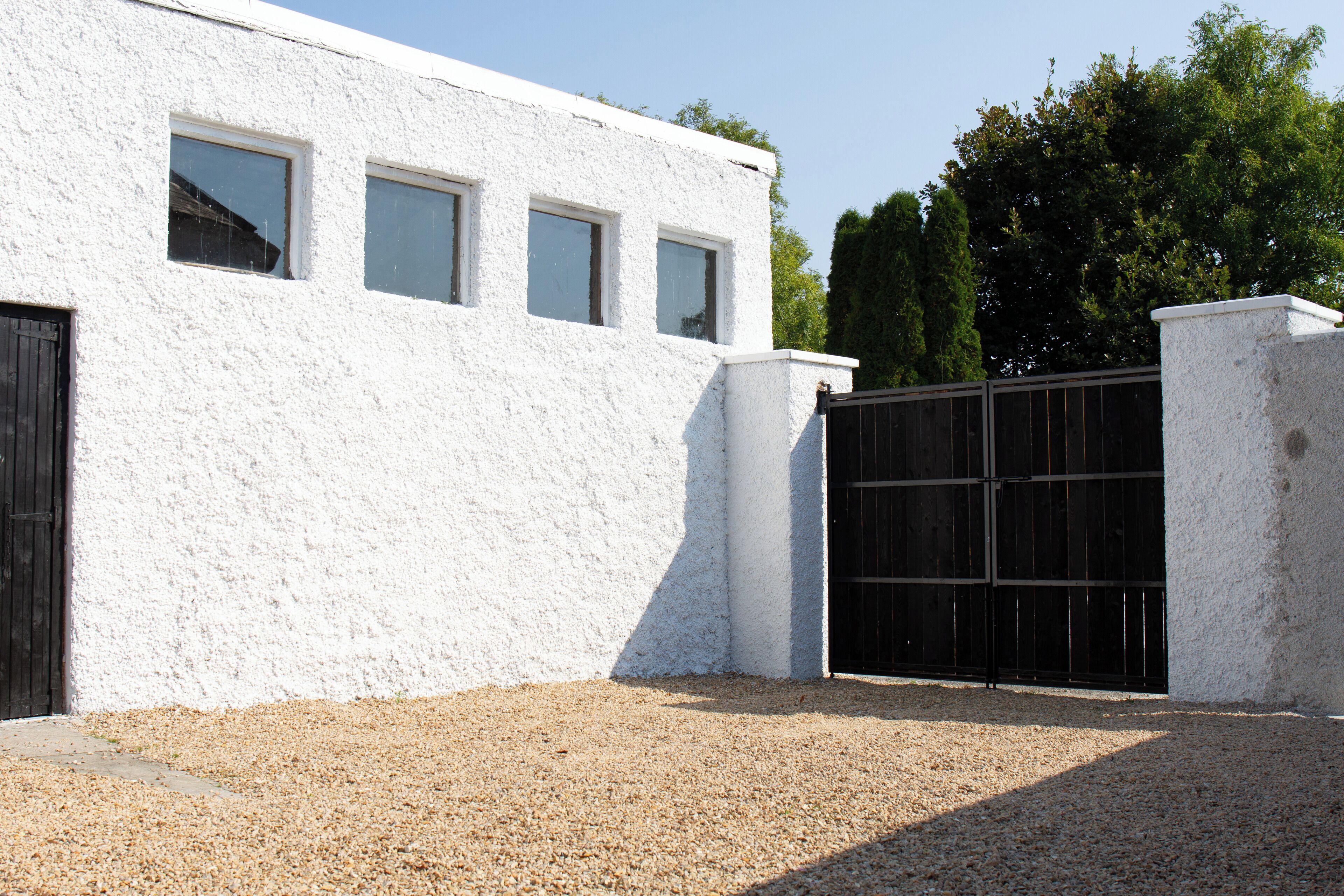 A building with a white exterior, a gravel driveway, and a black gate.