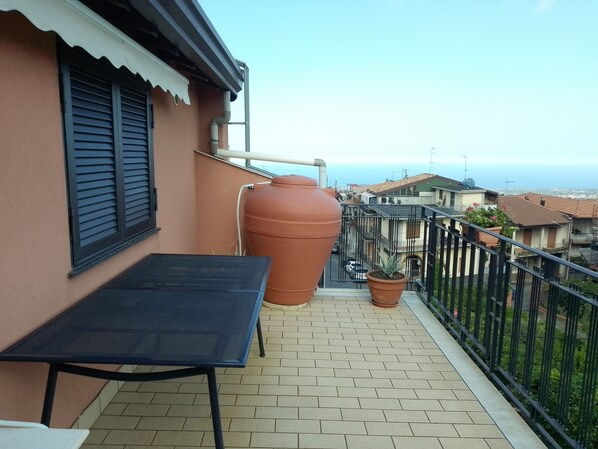 Un balcon avec une table, un grand pot en terre cuite et une petite plante en pot.