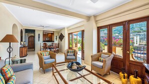 A spacious living area with wicker furniture, a dining table, and a view of a balcony with potted plants and flowers. - SUMMER PROMO: 6th Floor Corner Unit on the beach in Old Town; Rooftop Pool (Puerto Vallarta)