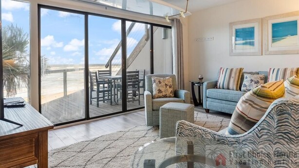 A spacious living area with a large sliding glass door leading to a balcony, a comfortable seating area with a sofa and armchairs, and a small table. - NEW LISTING - Oceanfront Condo ~ Excellent Location (Saint Augustine)