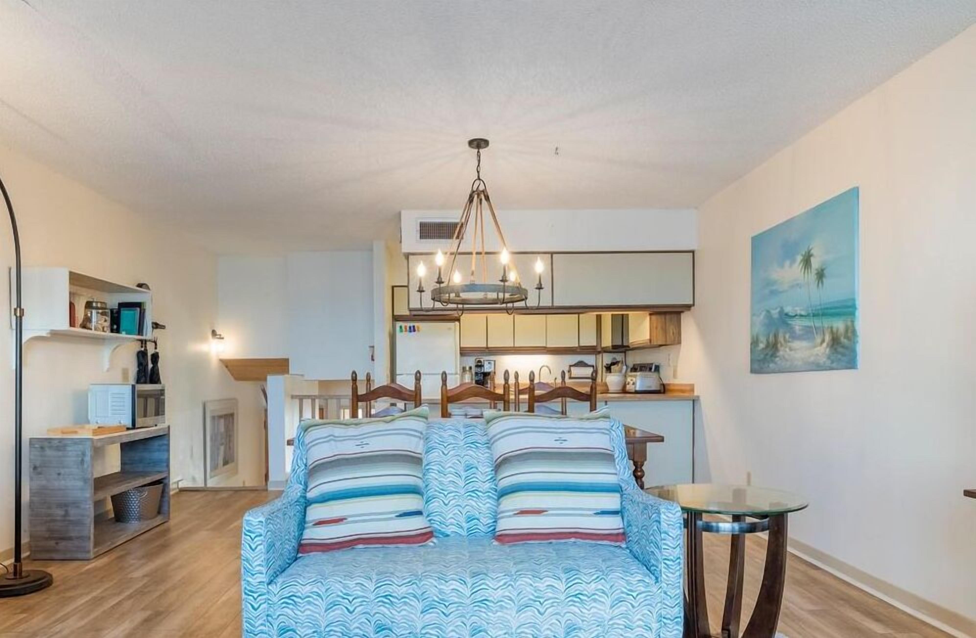 A cozy room with a bed, a small table, and a kitchenette in the background.