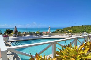A pool area with lounge chairs and umbrellas, overlooking a clear blue sea and a hilly landscape. - Paradise View - Stunning views near Dickenson Bay Beach in Antigua & Barbuda (Dickenson Bay Beach)