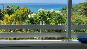 A covered outdoor area with a white railing, a blue cushion, and a view of the ocean and greenery. - Paradise View - Stunning views near Dickenson Bay Beach in Antigua & Barbuda (Dickenson Bay Beach)