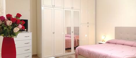 A bedroom with a bed, a wardrobe, a desk, and a vase of flowers.