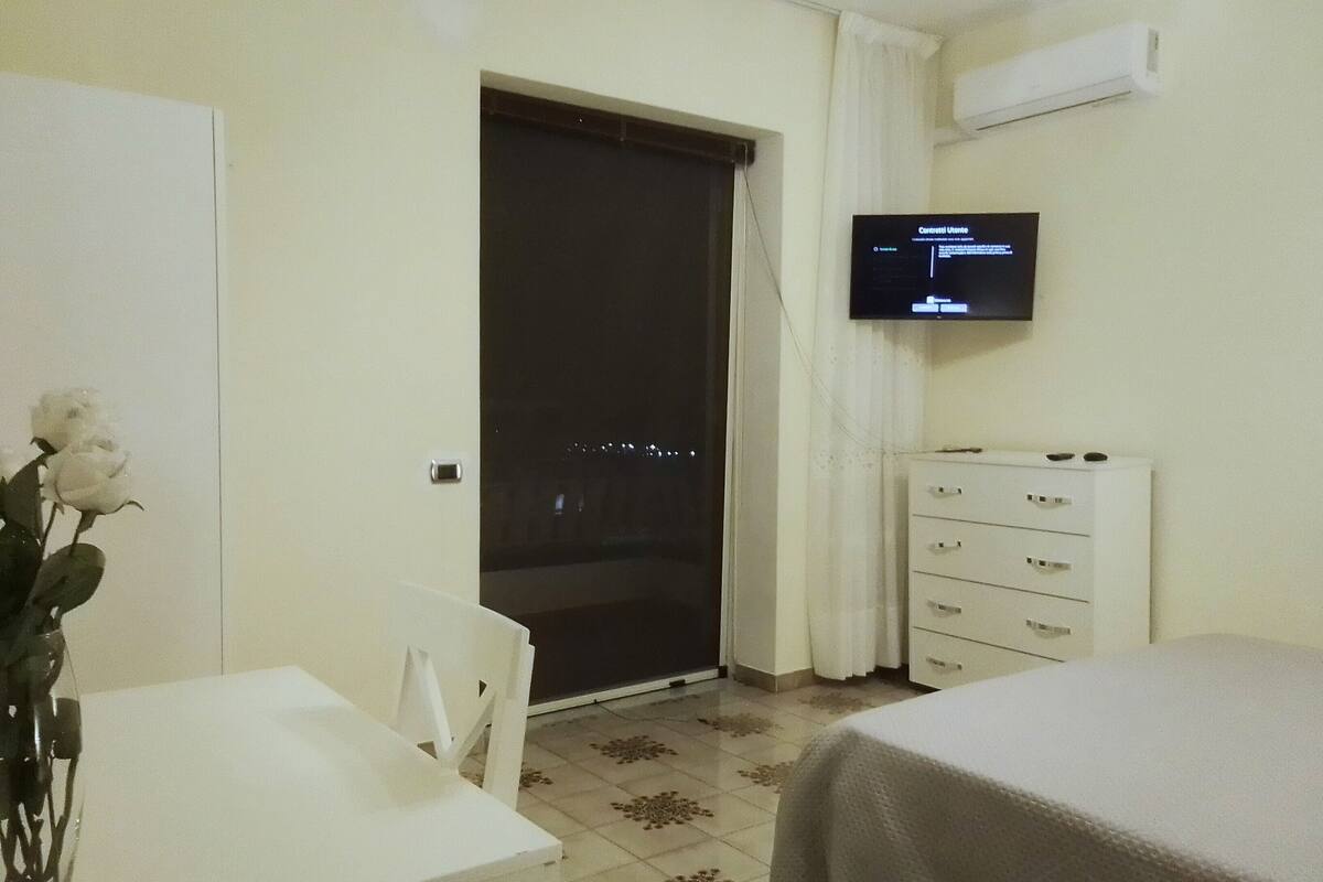Egy szállodai szoba, amelyben található egy ágy, egy íróasztal, egy szék, egy komód és egy televízió, amelyen a kezelőfelület látható.