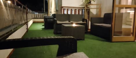 A balcony with outdoor furniture, a potted plant, and a view of the night sky.