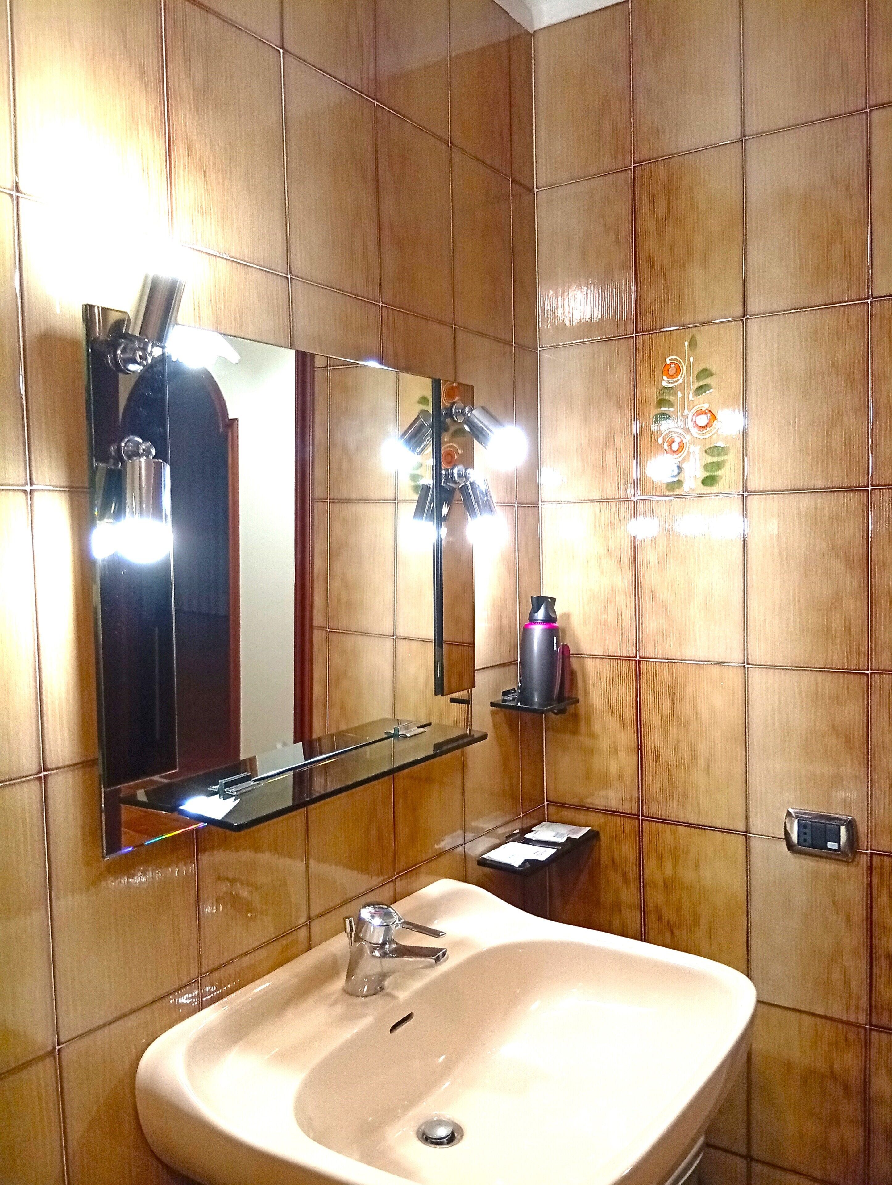 Een badkamer met een grote spiegel, een wastafel en een plank met toiletartikelen.
