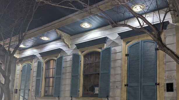 Um edifício com varanda, várias janelas com persianas e uma porta.