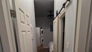 Um corredor estreito com piso de madeira, portas brancas e uma área de lavanderia visível ao fundo.