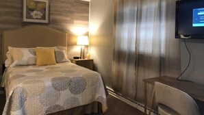 A hotel room with a bed, a nightstand, a lamp, a TV, and a chair.
