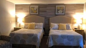 A hotel room with two beds, each with a headboard, bedside lamps, and a chair.