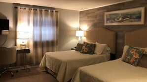 A hotel room with two beds, a desk, a chair, a lamp, and a painting on the wall.