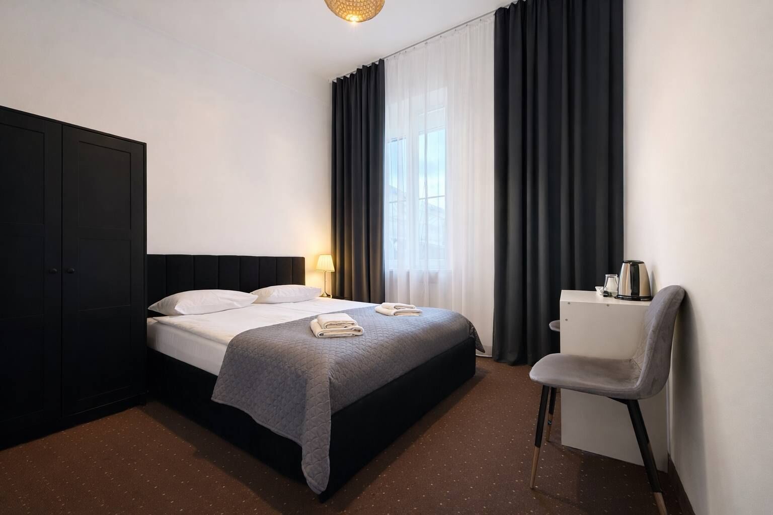 Habitació d'hotel amb llit, escriptori, cadira, armari i finestra amb cortines.
