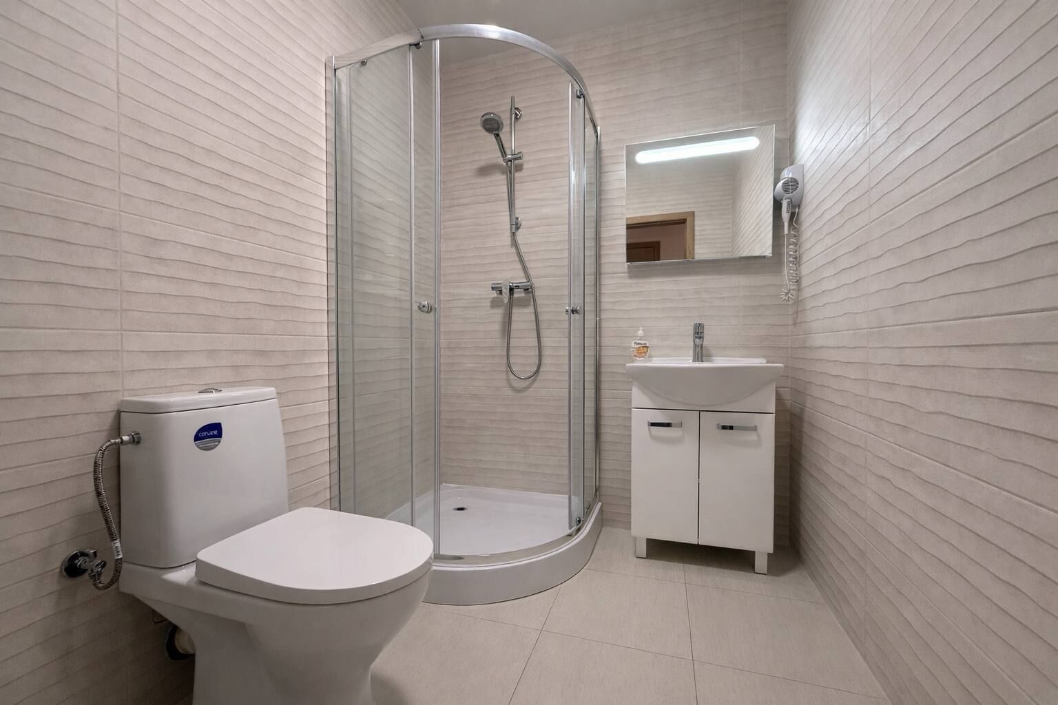 Et badeværelse med toilet, bruseniche, vask og spejl.