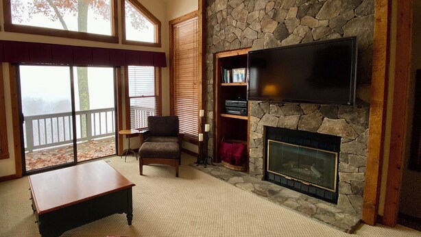 A spacious living room with a stone fireplace, a flat-screen TV, and large windows offering a view of the outdoors. - Mountain retreat! With spectacular views! (Burnsville)