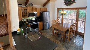 A kitchen with wooden cabinets, a stone backsplash, and a dining area with a table and chairs. - Mountain retreat! With spectacular views! (Burnsville)