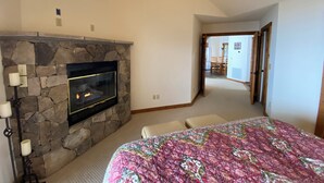 A bedroom with a stone fireplace, a ceiling fan, and a bed with a floral bedspread. - Mountain retreat! With spectacular views! (Burnsville)