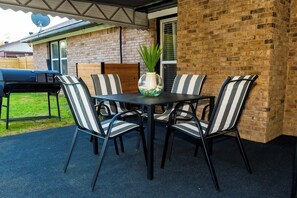 Un patio al aire libre con un muro de ladrillo, una mesa con sillas y una parrilla.