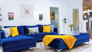 Ein modernes Wohnzimmer mit einem blauen Ecksofa, einer gelben Decke und einem gemusterten Teppich.