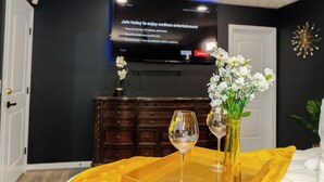 Ein Zimmer mit Fernseher, der eine Werbung zeigt, einer Holzkommode, einem gelben Tisch mit einem Weinglas und einer Blumenvase.