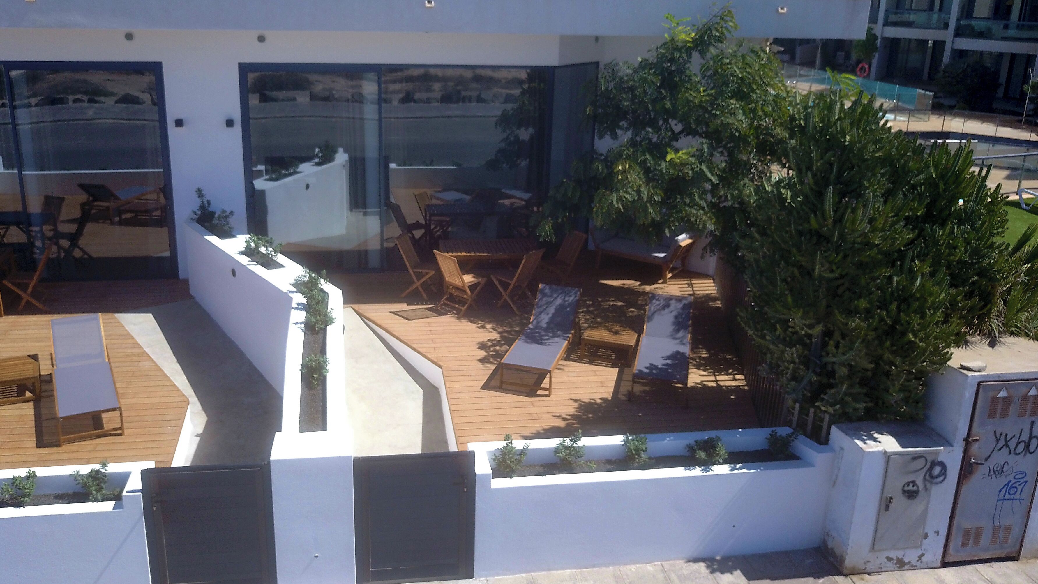 A rooftop terrace with wooden flooring, lounge chairs, and a large tree.