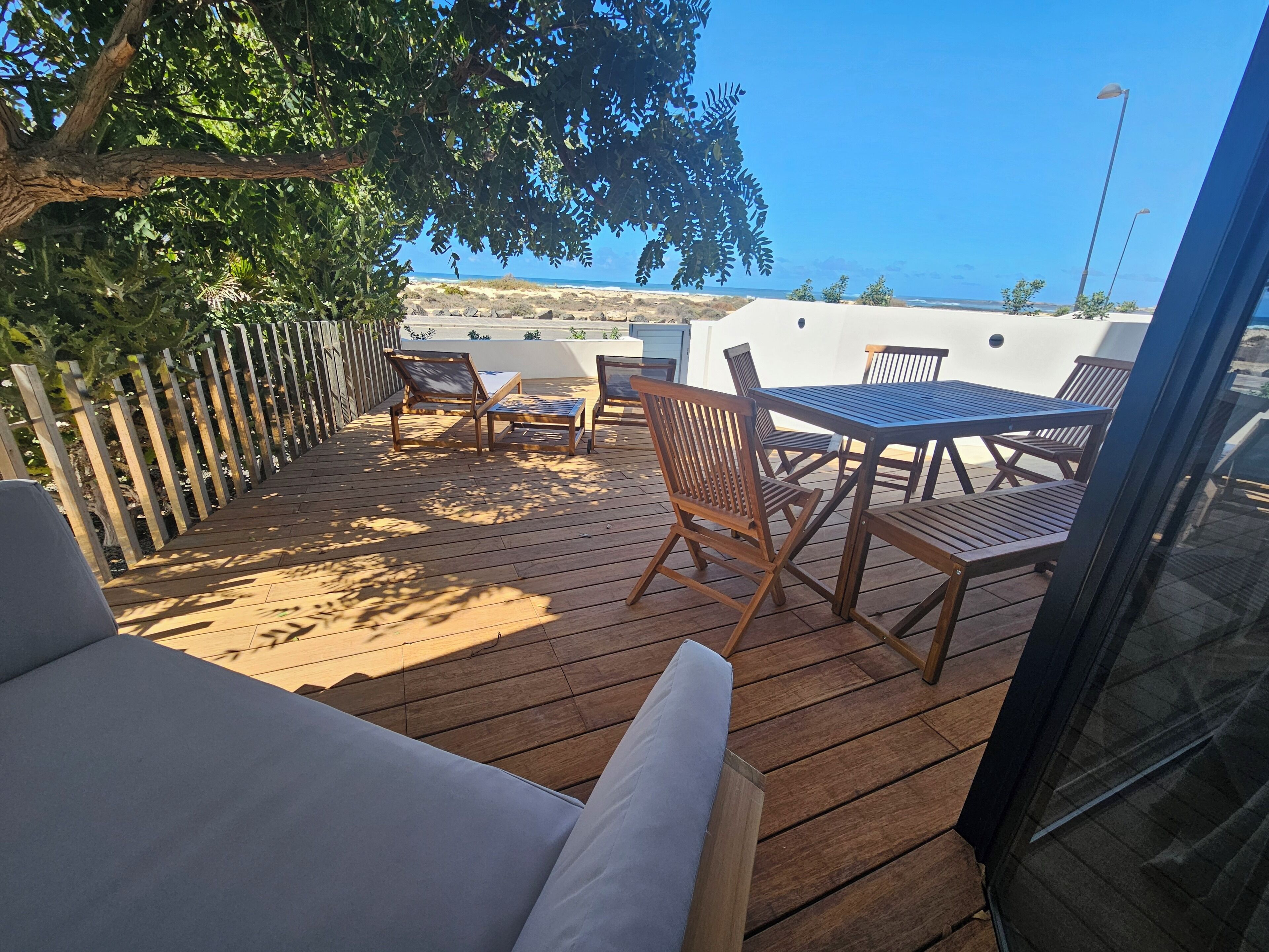 Een houten terras met buitenmeubilair, zoals een tafel en stoelen, met uitzicht op de kust.