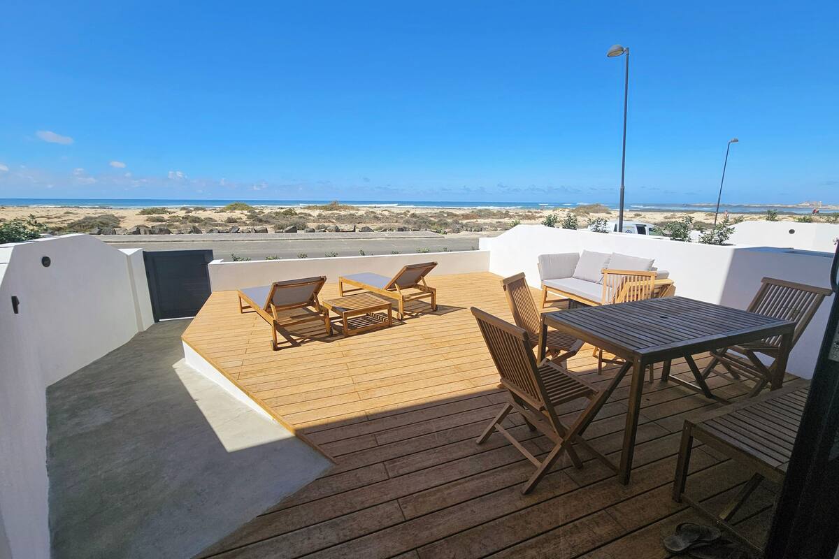 A rooftop terrace with wooden furniture, a table, and a view of the beach.