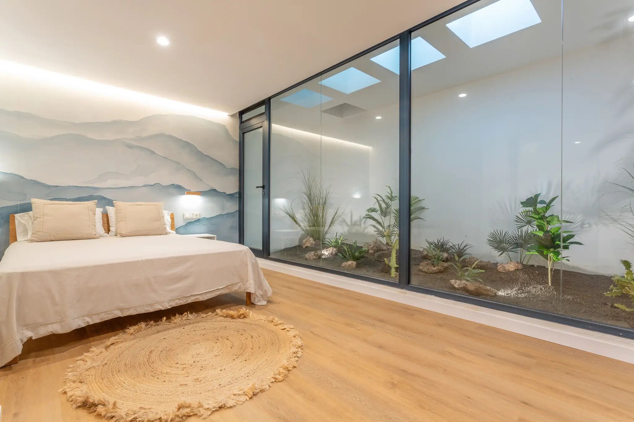 A bedroom with a bed, a large window with a view of a rock garden, and a wall with a mountain mural.