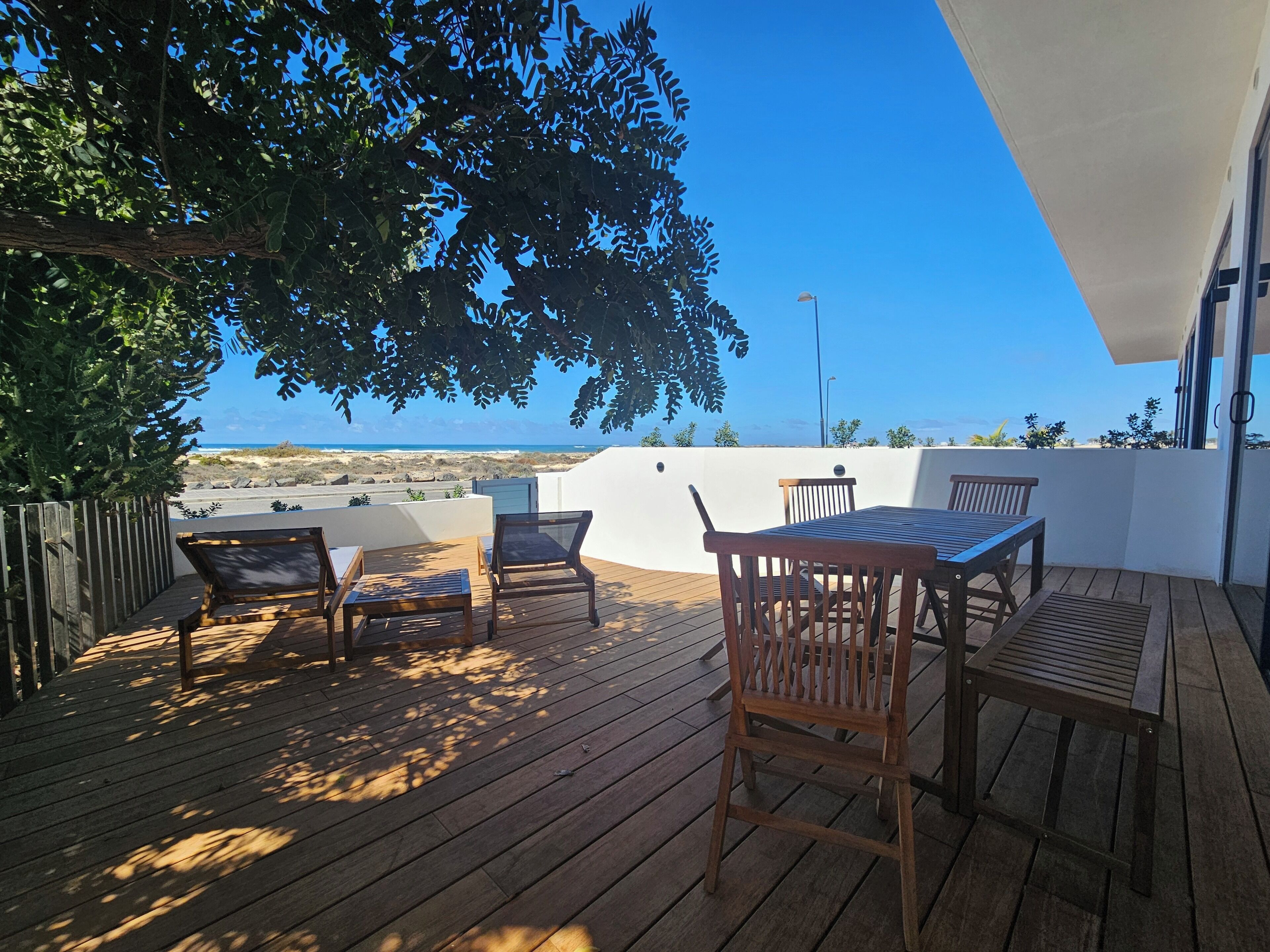 A wooden deck with a table and chairs, overlooking a beach.