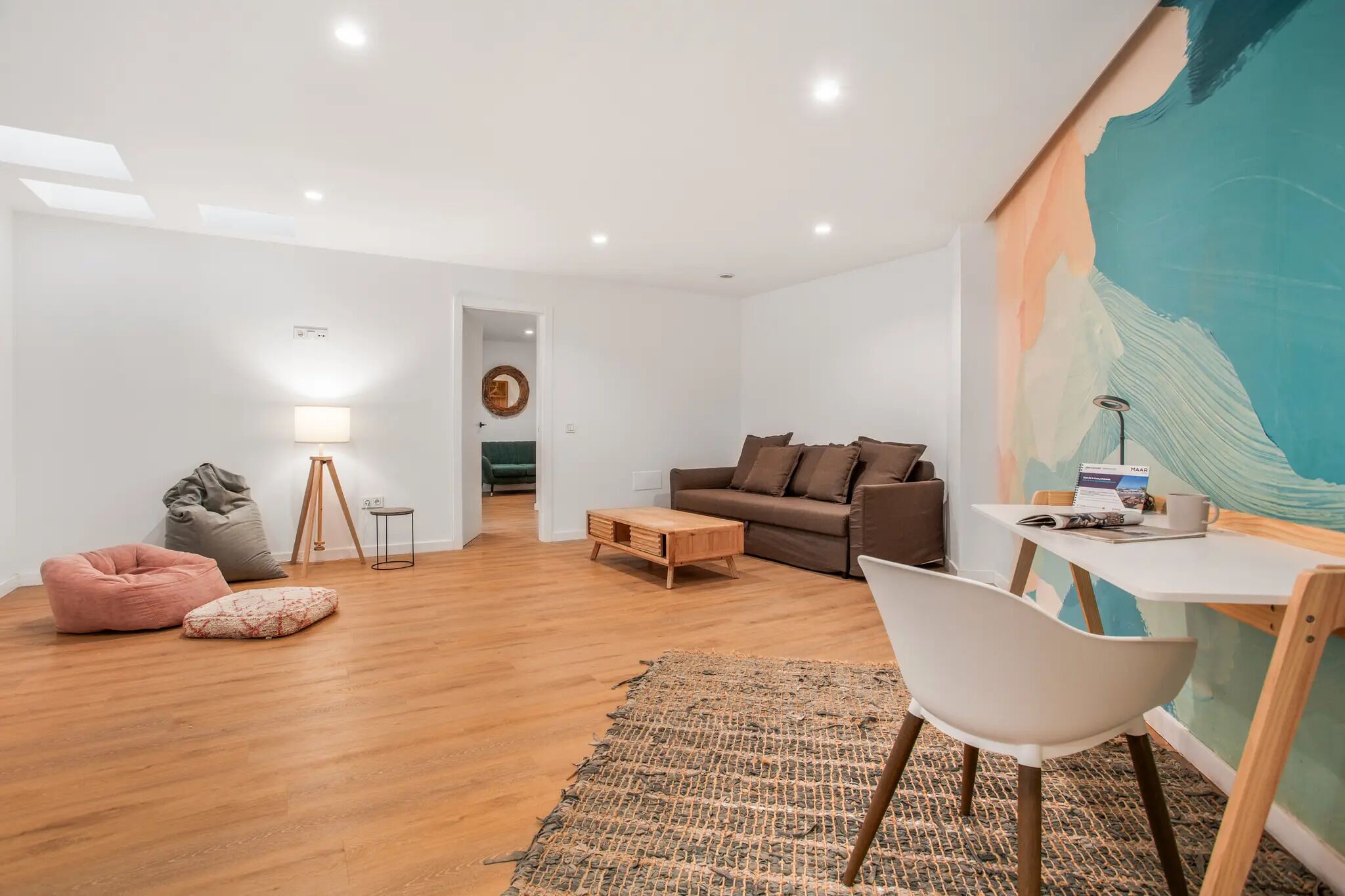 Un salon moderne avec un canapé, une table basse, un fauteuil blanc, un tapis et un tableau accroché au mur.