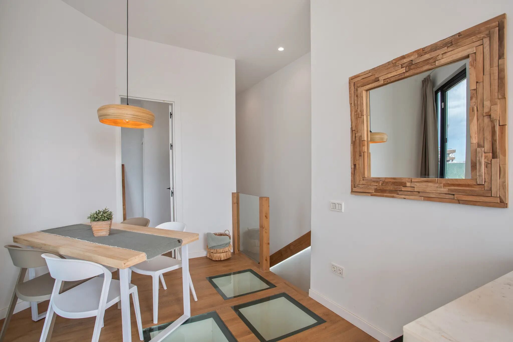 Ein Essbereich mit Holztisch, weißen Stühlen, einer Pendelleuchte und einem Spiegel an der Wand.