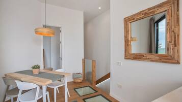Ein Essbereich mit Holztisch, weißen Stühlen, einer Pendelleuchte und einem Spiegel an der Wand.