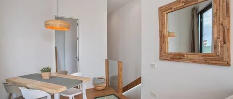 A dining area with a wooden table, white chairs, a hanging light fixture, and a mirror on the wall.