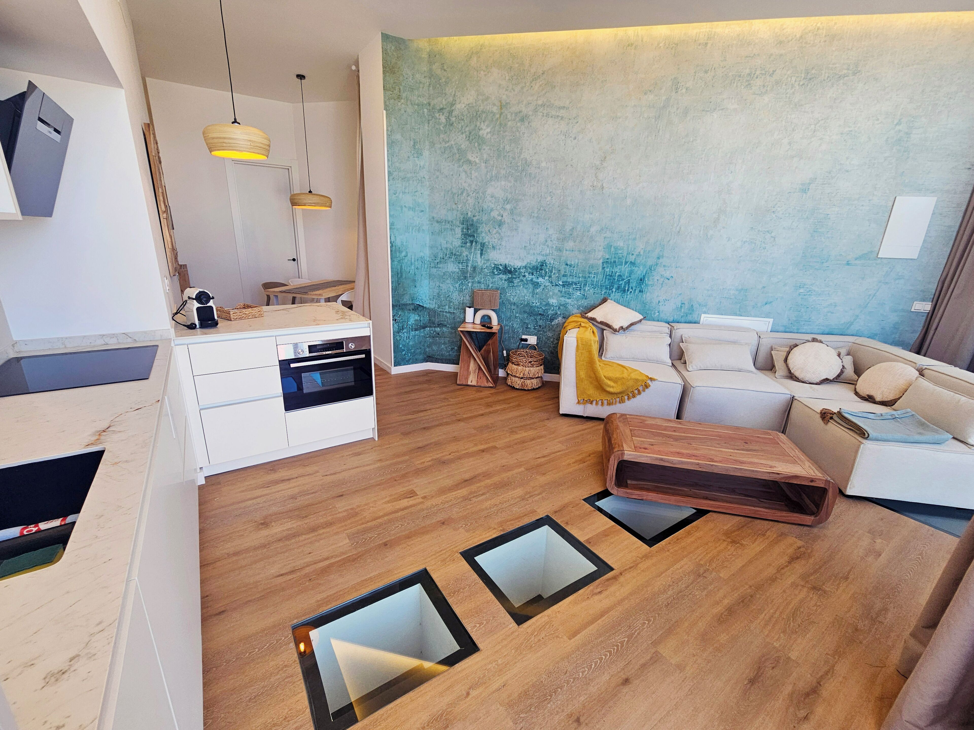 Un espace de vie moderne comprenant une cuisine, un canapé blanc et une table basse en bois.