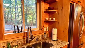A kitchen with a double sink, wooden cabinets, a stainless steel refrigerator, and a window with a view of trees. - NEW! HOT TUB; FIREPIT; FAST WIFI; Near Blue Ridge, Blairsville, Folk School (Murphy)