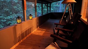 A wooden deck with a rocking chair and a lamp, overlooking a forested area. - NEW! HOT TUB; FIREPIT; FAST WIFI; Near Blue Ridge, Blairsville, Folk School (Murphy)