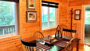 A wooden cabin interior with a dining table, chairs, framed pictures, and a chandelier. - NEW! HOT TUB; FIREPIT; FAST WIFI; Near Blue Ridge, Blairsville, Folk School (Murphy)