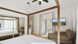 Un dormitorio con una cama grande, un sofá, un televisor y una puerta corredera que da a un baño.