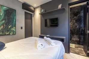 A modern hotel room with a large bed, a flat-screen TV, a marble-tiled shower area, and a painting on the wall.