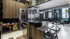 Een moderne keuken met inbouwapparatuur, een eetgedeelte met zwarte stoelen en een groene bank in de woonkamer.