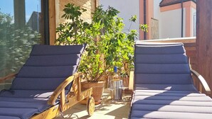 Eine Holzbalkendecke, zwei Lounge-Sessel, ein Topfpflanze und ein Gebäude im Hintergrund.